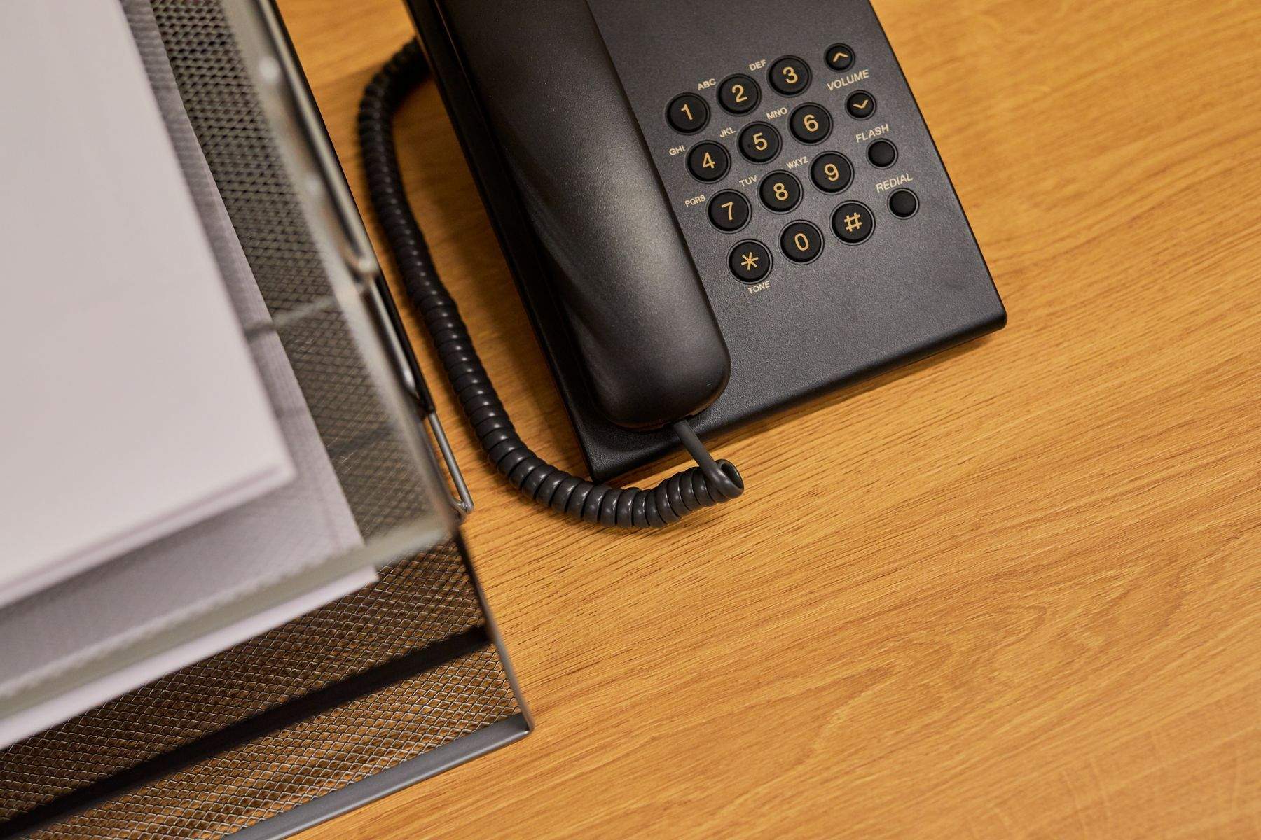 Telefon fix negru pe un birou din lemn, lângă un suport cu documente