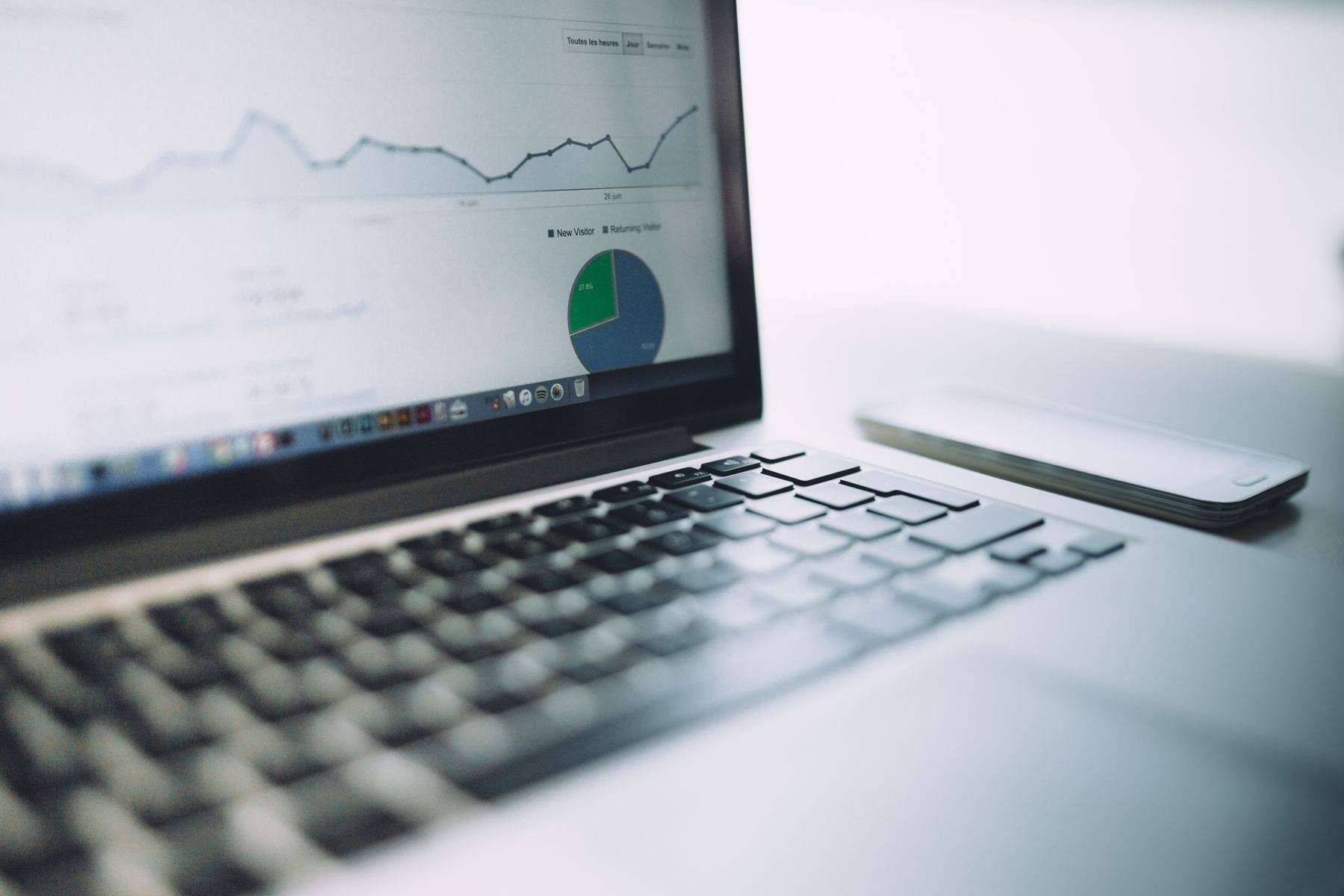Laptop pe un birou alb, cu grafice de statistici pe ecran
