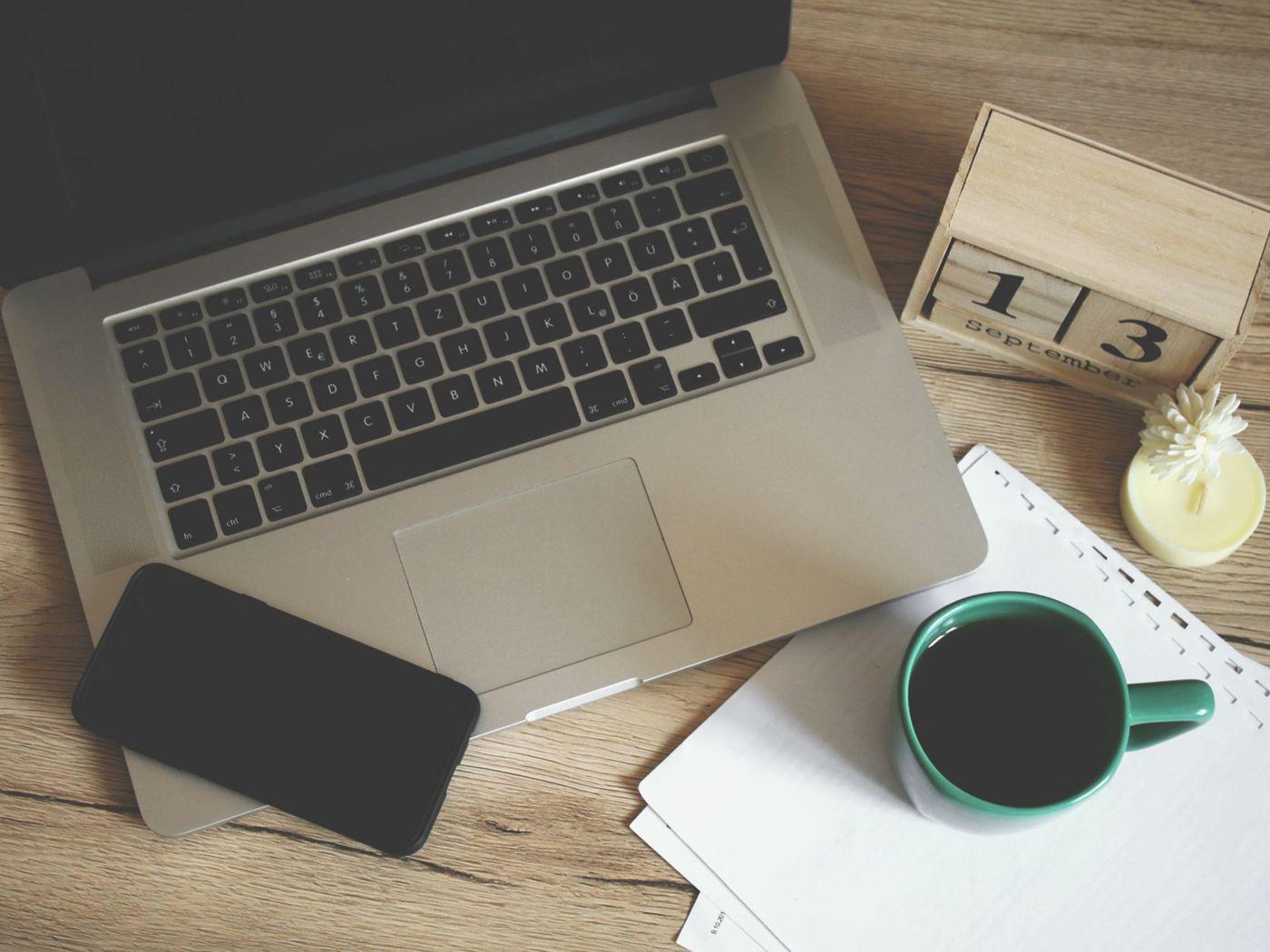 Laptop, telefon, cană de cafea și calendar de birou pe o masă din lemn