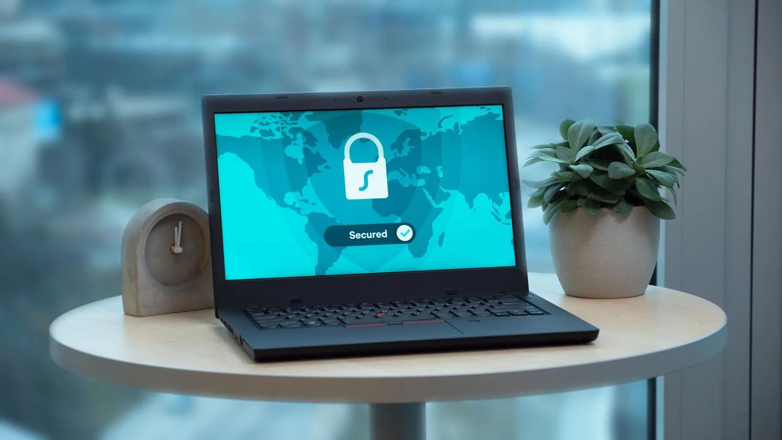 Laptop pe o masă, cu un lacăt și textul „Secured” pe ecran