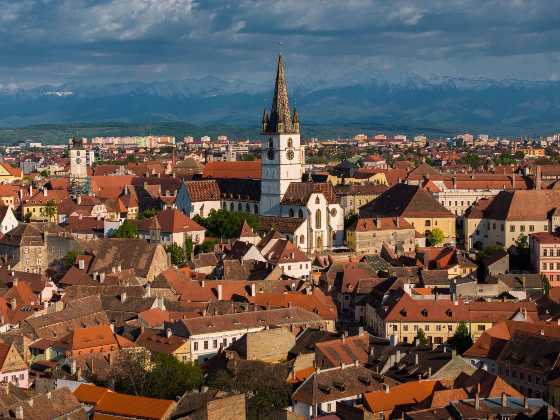 Centrul istoric al Sibiului văzut de sus, cu acoperișuri roșii și Munții Făgăraș în fundal
