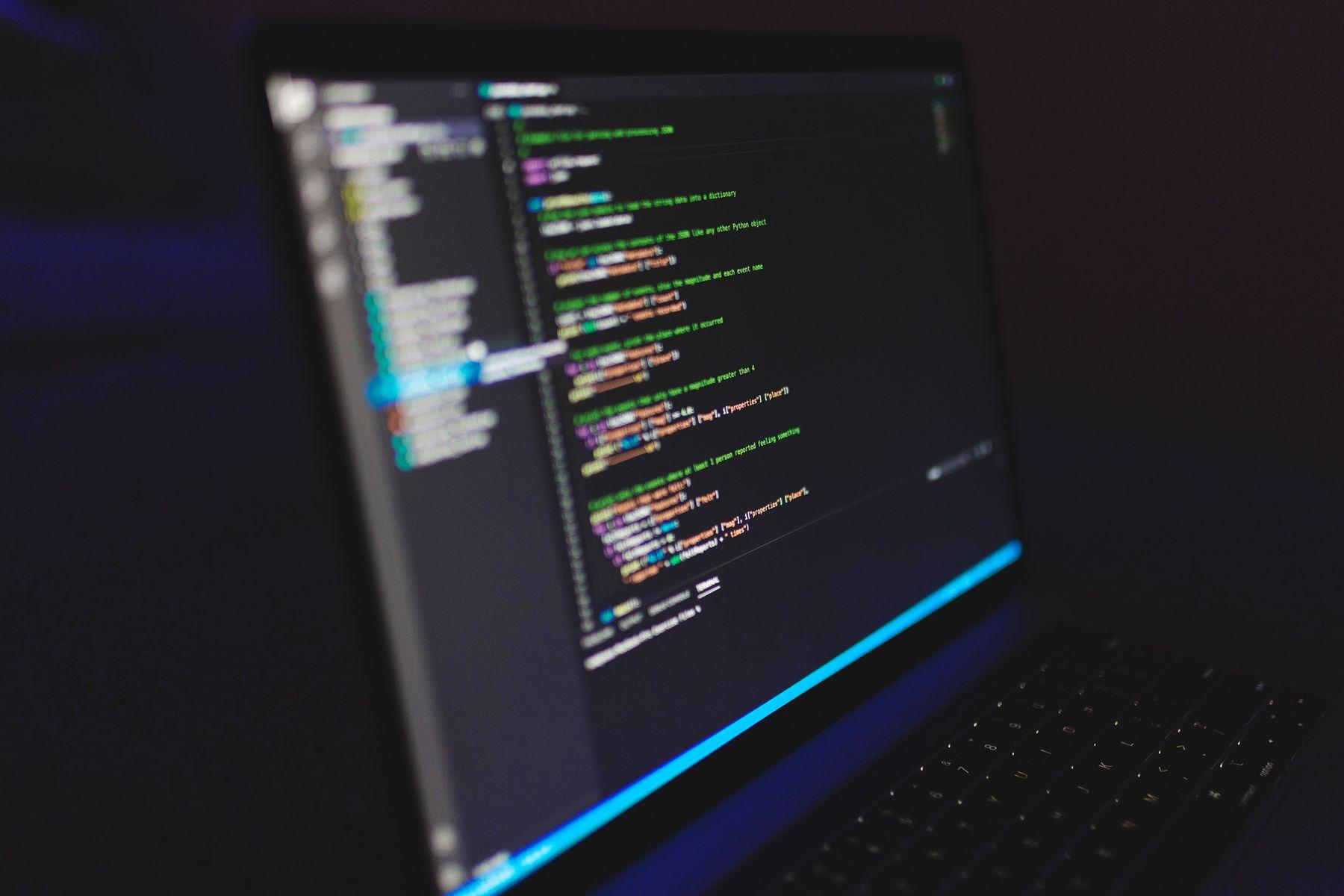 Laptop cu cod sursă pe ecran, într-o cameră întunecată