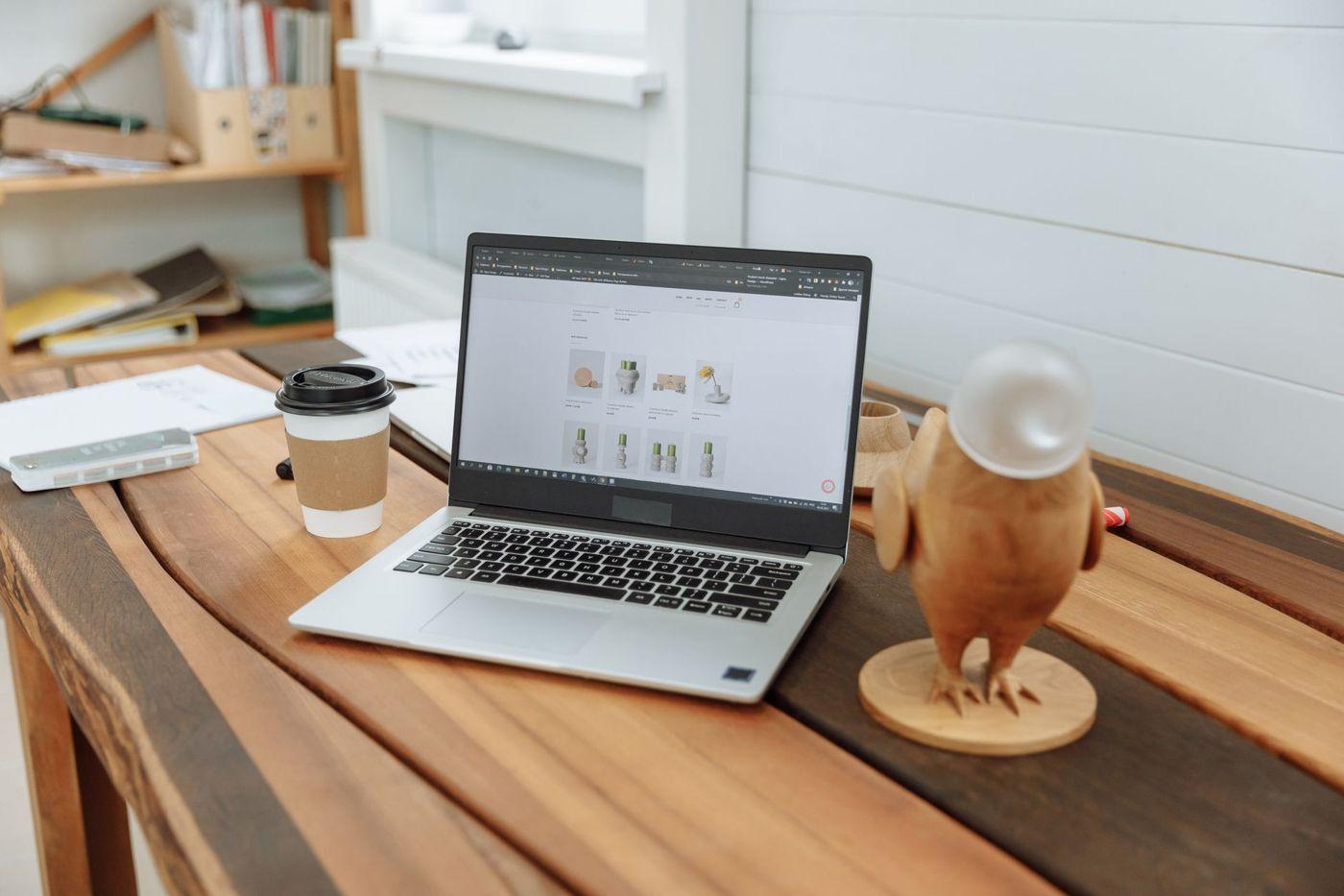 Birou cu laptop, cană de cafea și o figurină din lemn